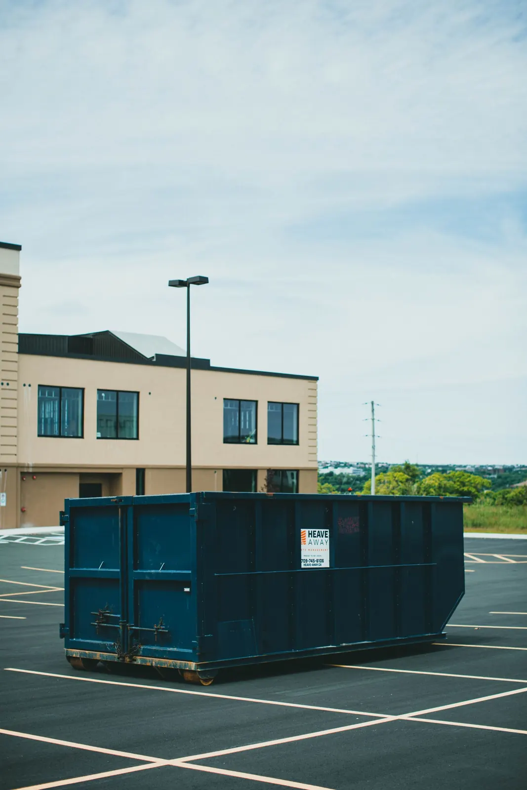 Open-top roll-off container in a paved commercial parking area.